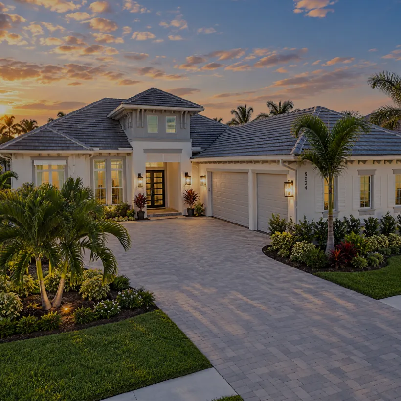 New Construction Homes in Naples, Florida: single-story estate home at dusk with lit entry and paver drive in Caymas, Naples, Florida