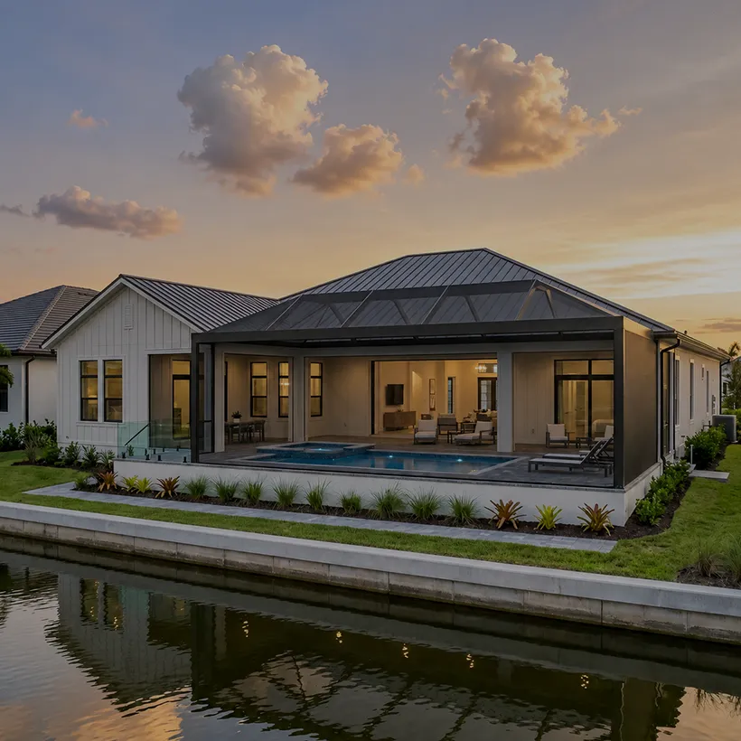 Waterfront home at dusk with screened pool and lit interior reflected in the water at Isles of Collier Preserve, Naples, Florida