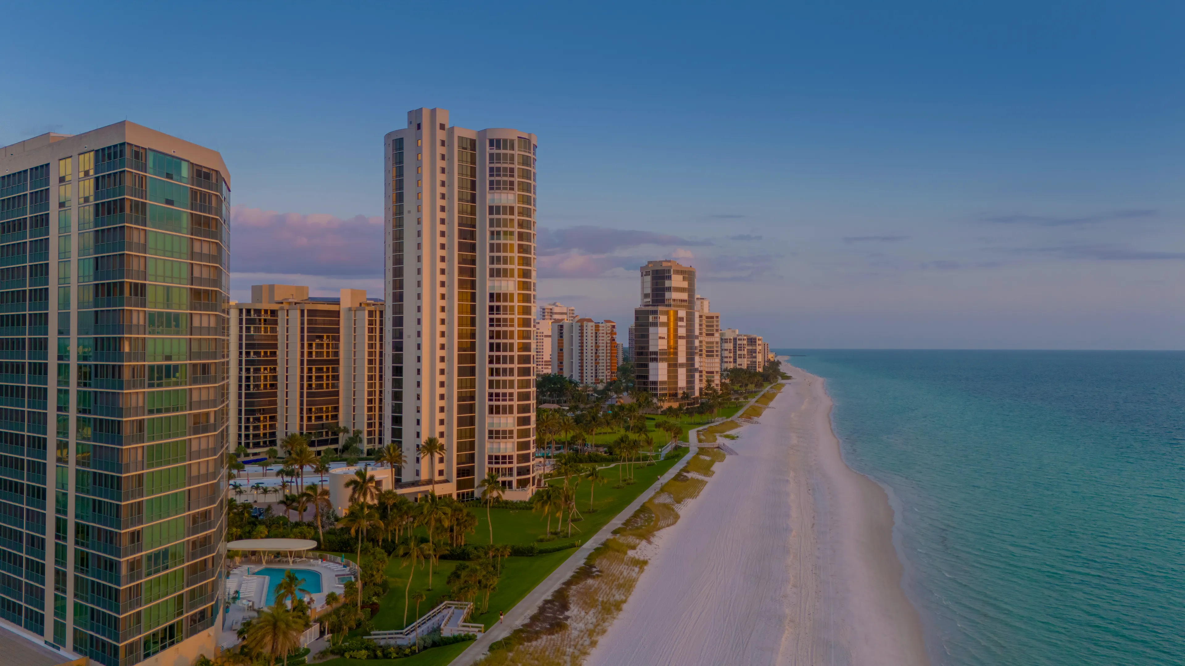 Aerial view of beachfront condominium towers along the Gulf of Mexico in Naples, Florida, at dusk