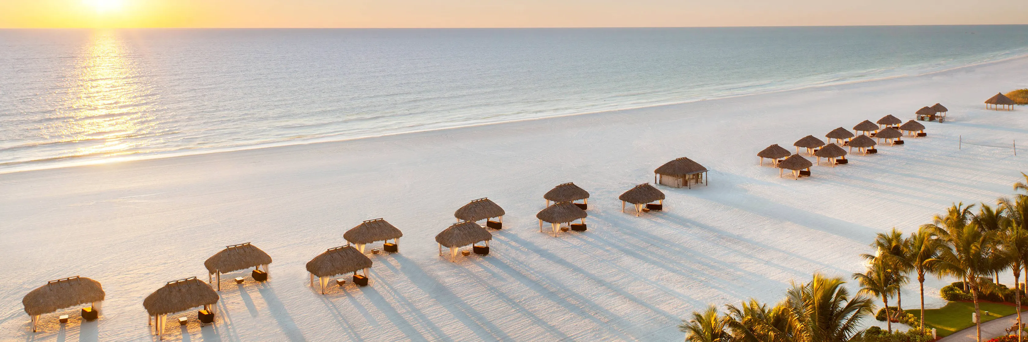 Thatched beach cabanas on white Gulf sand at sunset, the Southwest Florida beach life near Marco Island