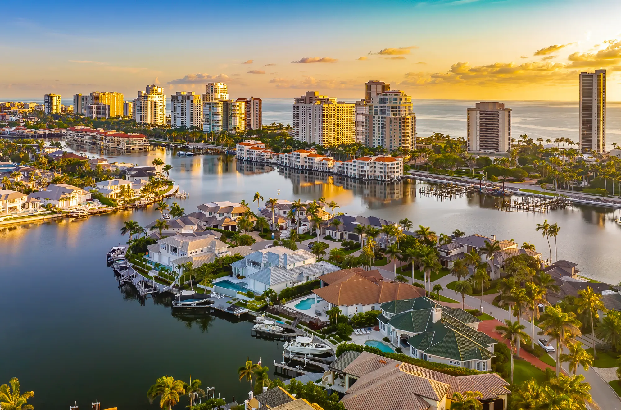 Canal-front homes with boat docks and condominium towers along the Gulf of Mexico in Park Shore, Naples, Florida, at sunset