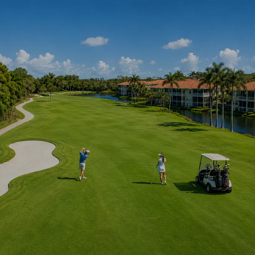 Condos with Boat Docks in Naples, Florida: golfers on a fairway beside a lake and condominium buildings at Windstar on Naples Bay, Naples, Florida