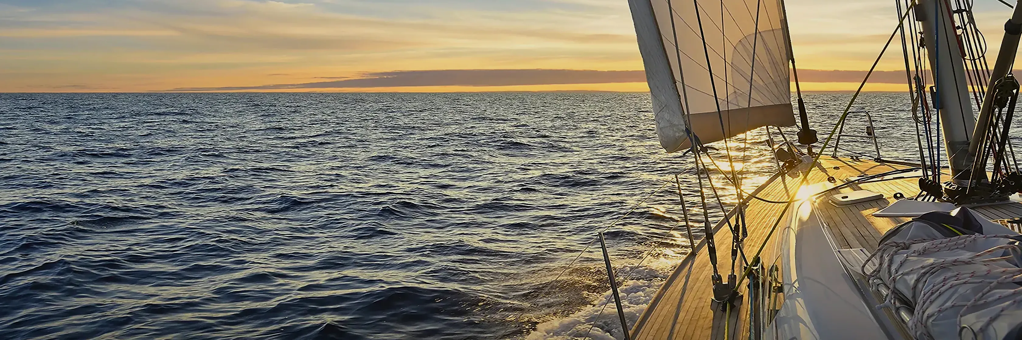 View along the deck of a sailboat under sail on open water at sunset