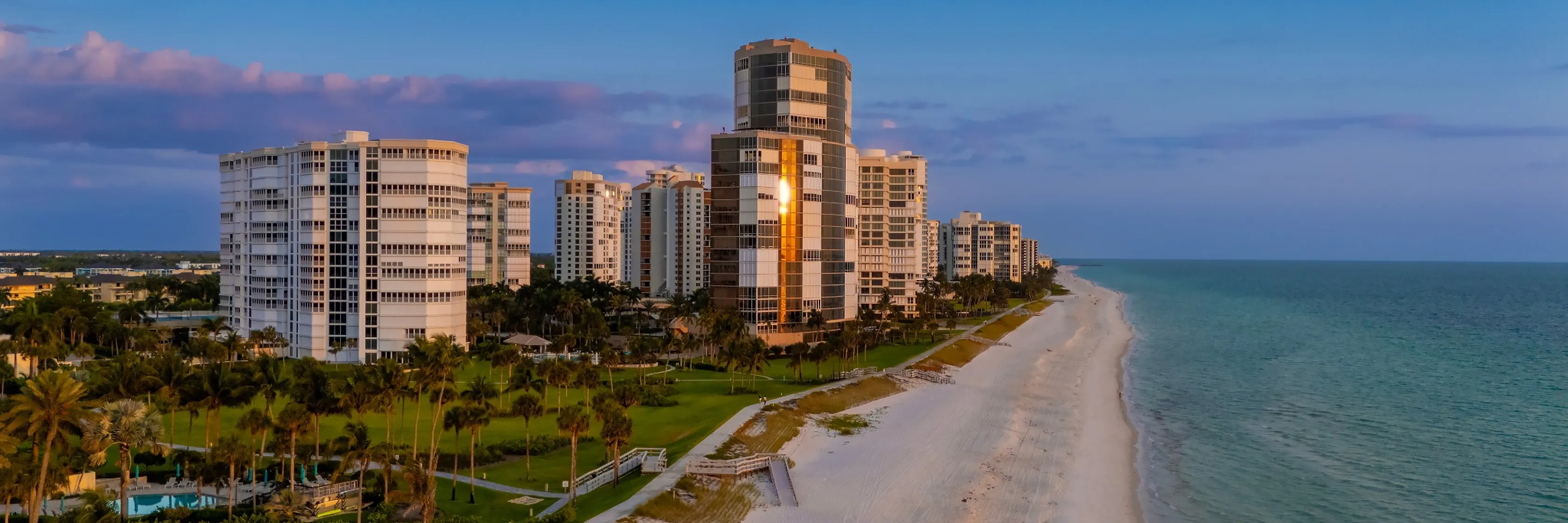 High-rise condominium towers along a white-sand beach and the Gulf of Mexico at dusk in Naples, Florida