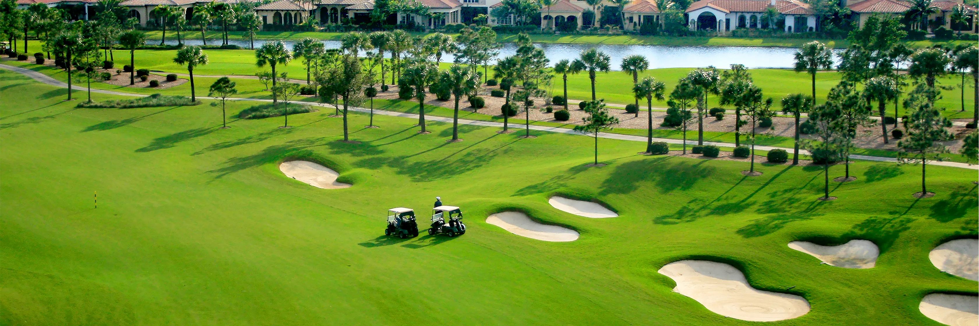 Golf carts on a fairway lined with palms and lakeside homes in a Naples, Florida golf community