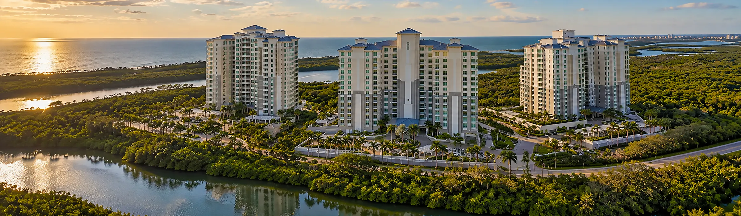 Aerial view at sunset of three high-rise condominium towers above mangroves and a lagoon, with the Gulf of Mexico beyond, in Naples, Florida