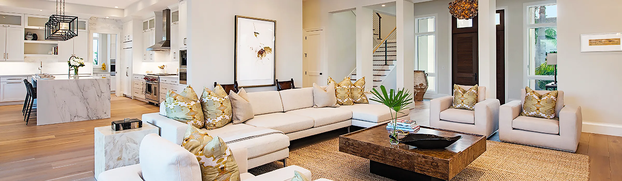 Open-plan living room and kitchen of a new home in Naples, Florida, with a marble waterfall island and white oak floors